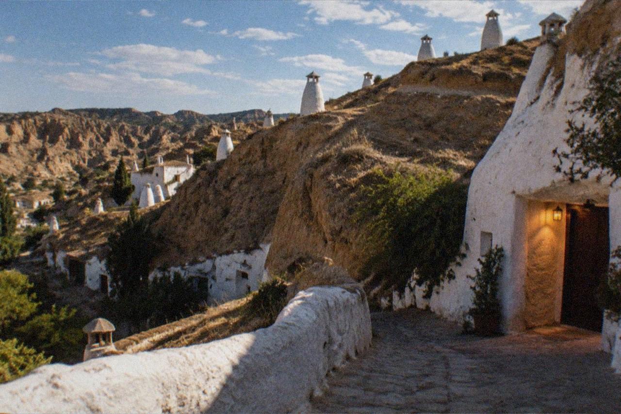 A whitewashed cave house doorway carved into the hillside of Sacromonte at dusk, with warm light spilling onto the stone path