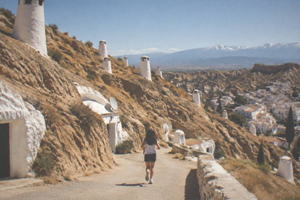 The Sacromonte hillside at golden hour, rows of white cave houses climbing above the city with the Sierra Nevada in the far distance
