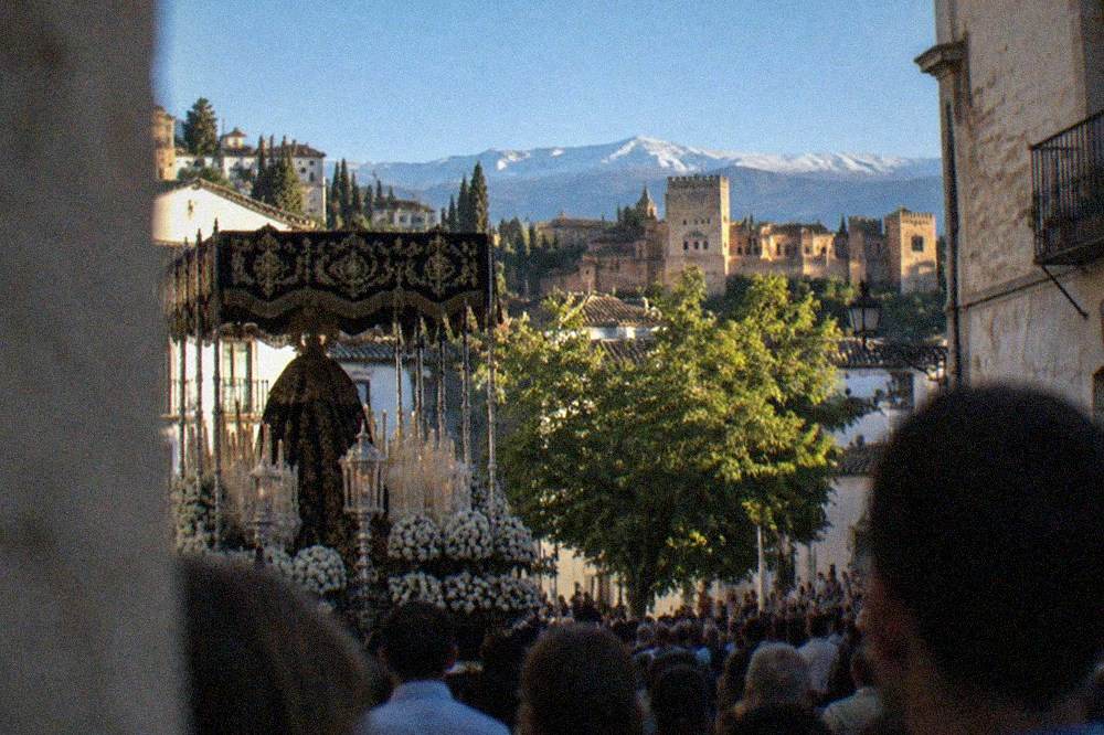 A decorated processional float carried through a crowded square with onlookers lining the walls