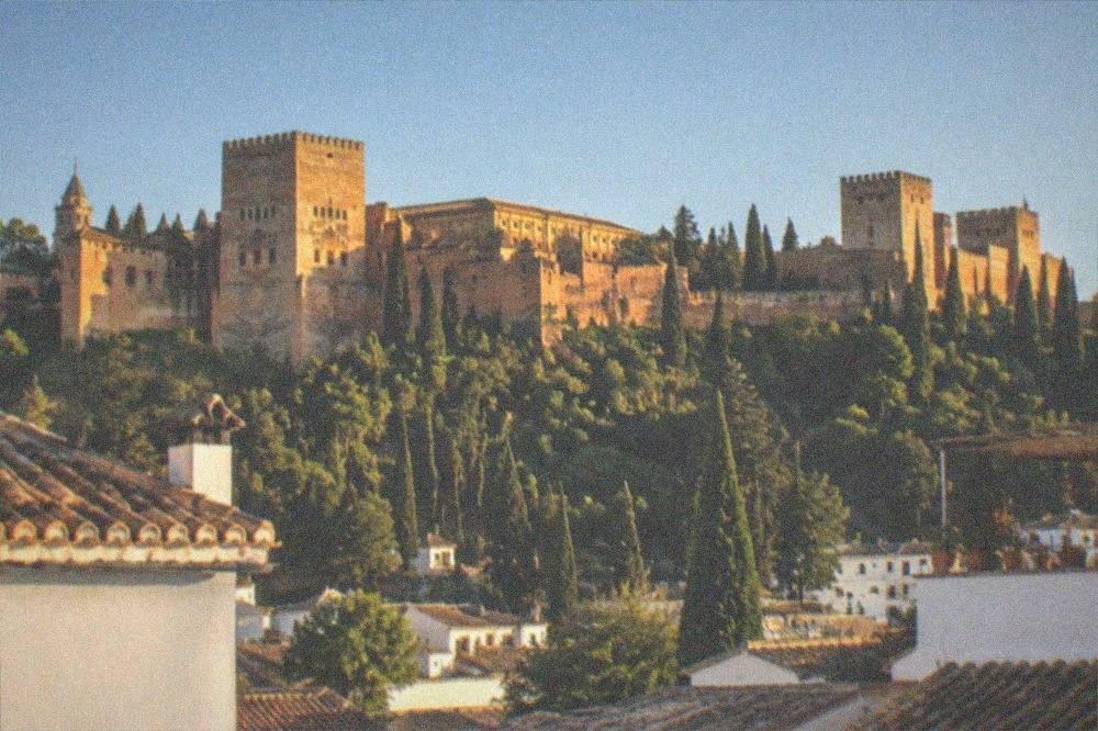 The Alhambra palace walls and towers glowing above Granada at dusk, seen from a city rooftop