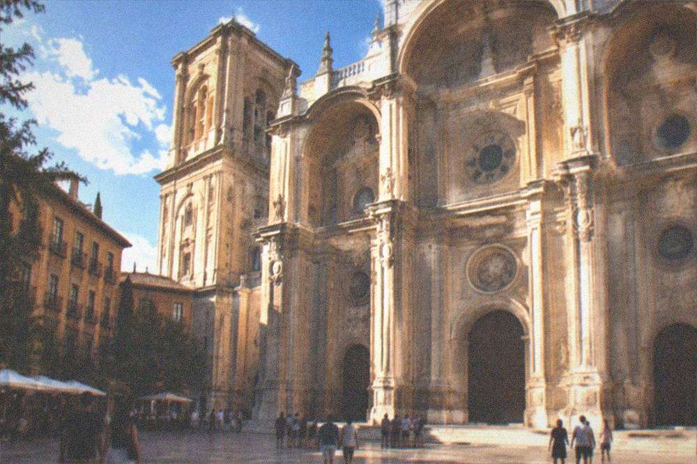 The ornate baroque facade of Granada Cathedral lit in the evening with people gathered in the square