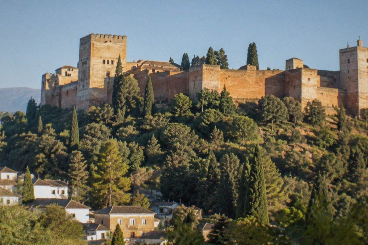 The Alhambra palace complex seen across a valley from a hillside viewpoint in Granada at golden hour
