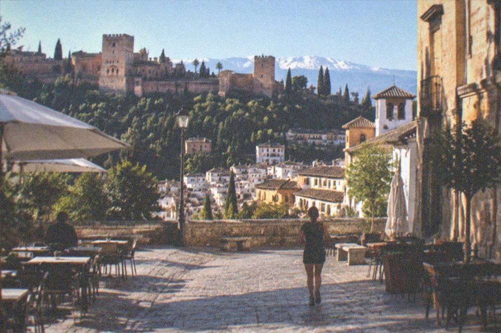 A plaza with outdoor tables and historic buildings in central Granada in the evening