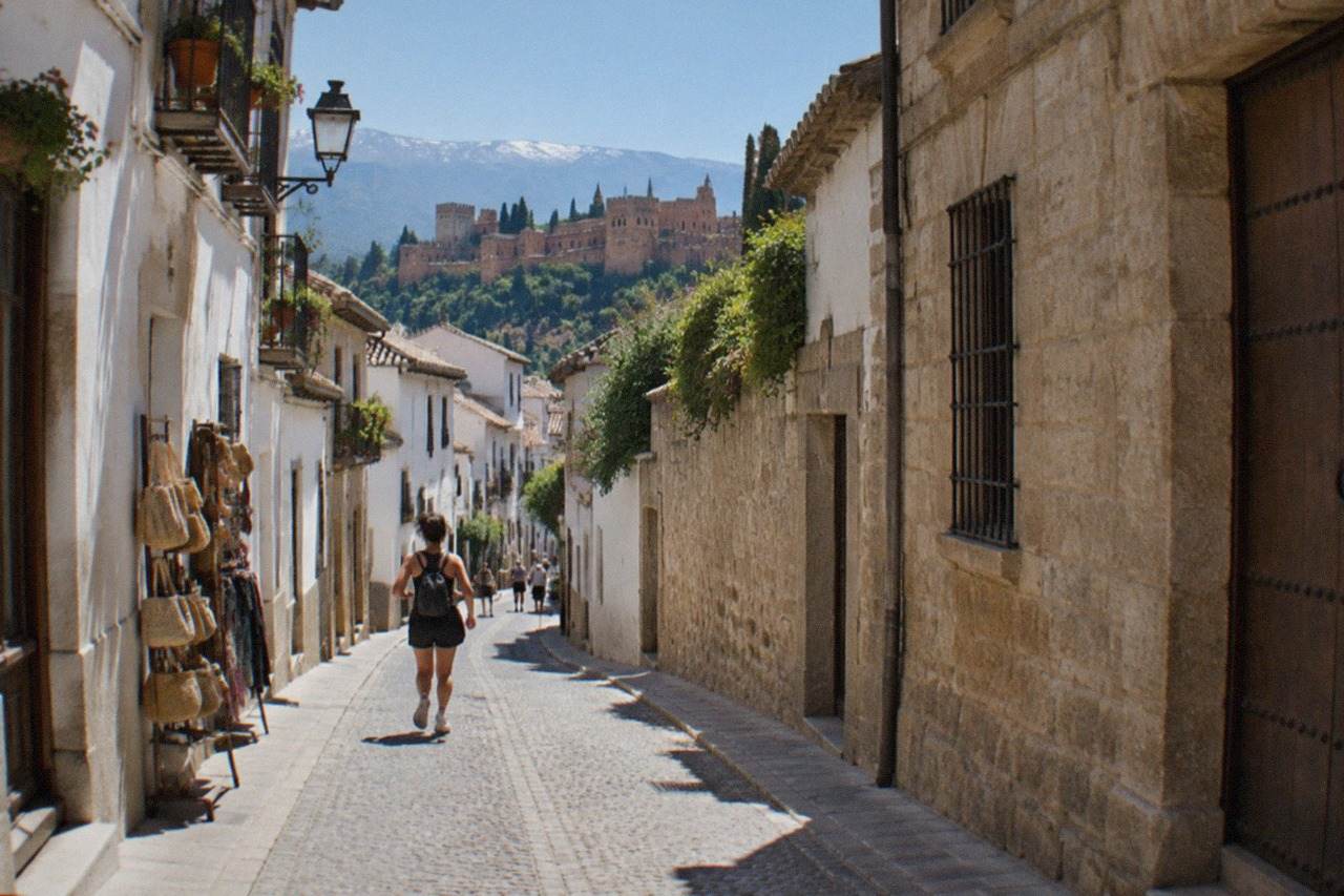 A narrow Granada shopping street with small storefronts and stone buildings under a clear sky