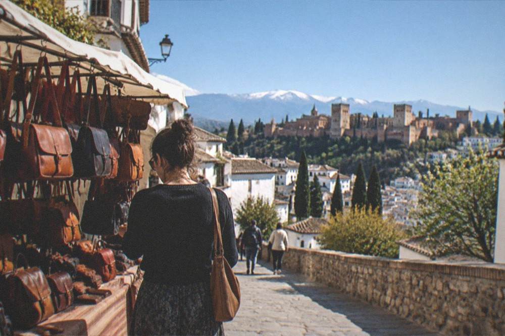 A shopper comparing handcrafted leather bags displayed on a market stall in Granada