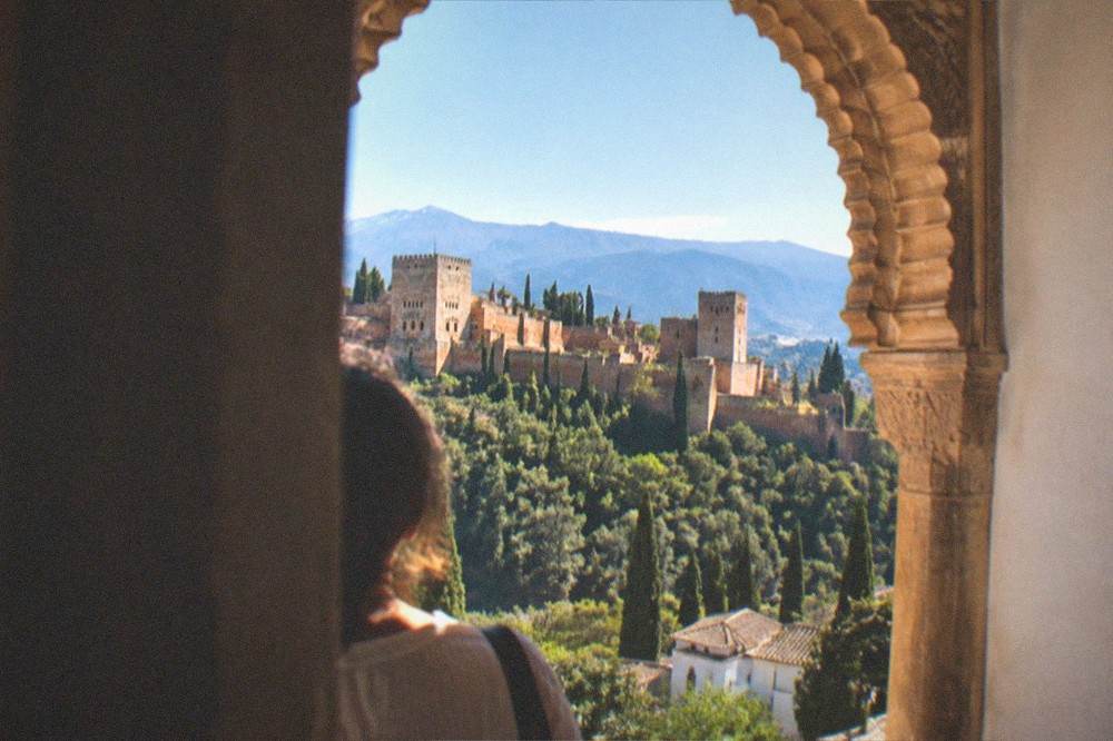 An ornate arched window framing the gardens and distant mountains from inside the palace