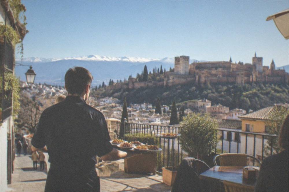 A waiter carrying several small tapas plates to a table in a Granada bar
