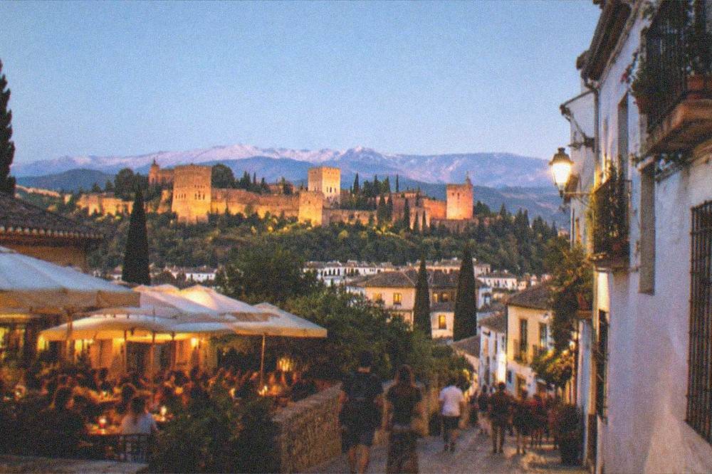 An evening street in Granada with lit bar terraces and people walking