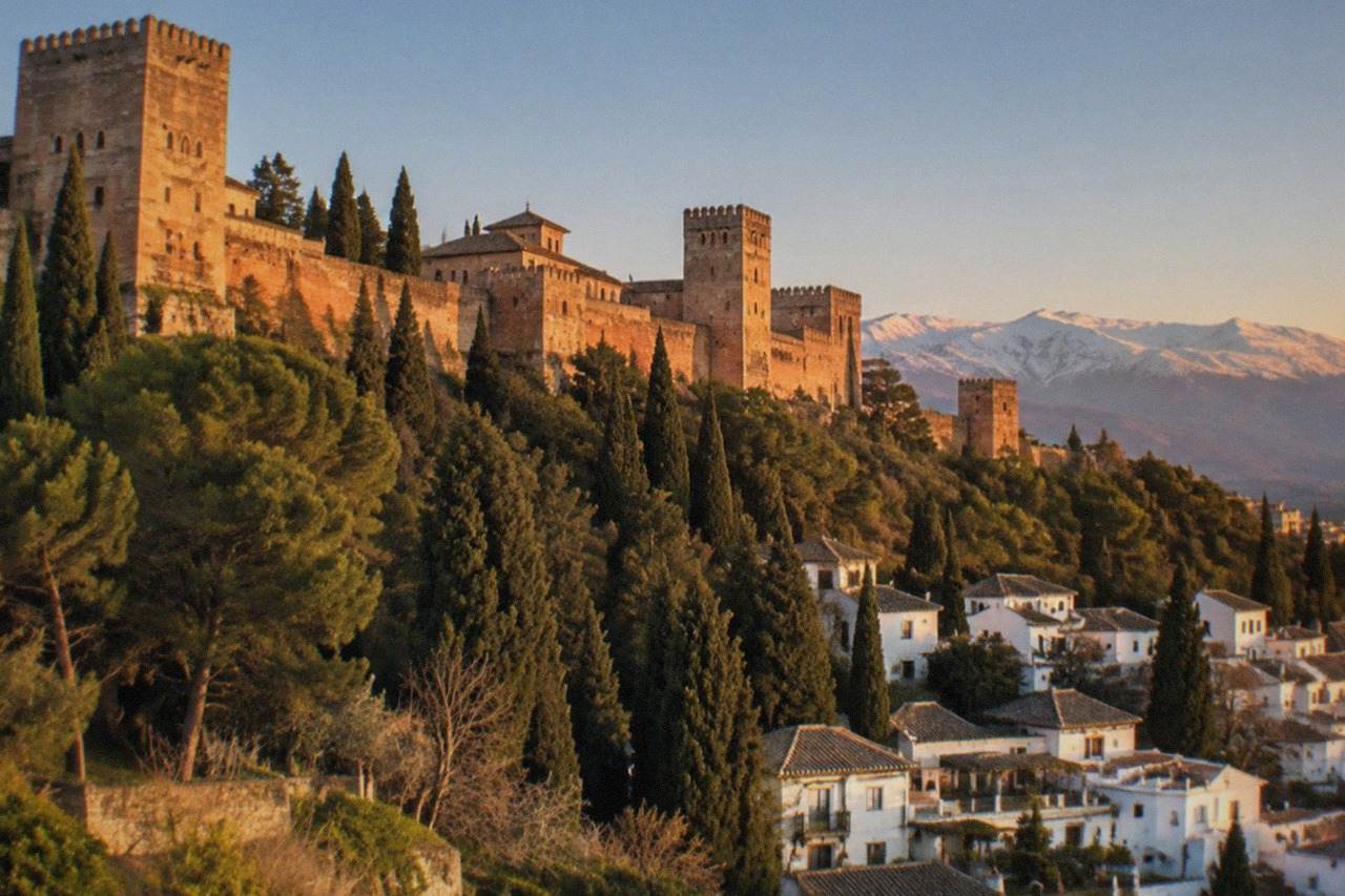 White houses of the Albaicin district on a hillside with the Alhambra and Sierra Nevada in the background at sunset