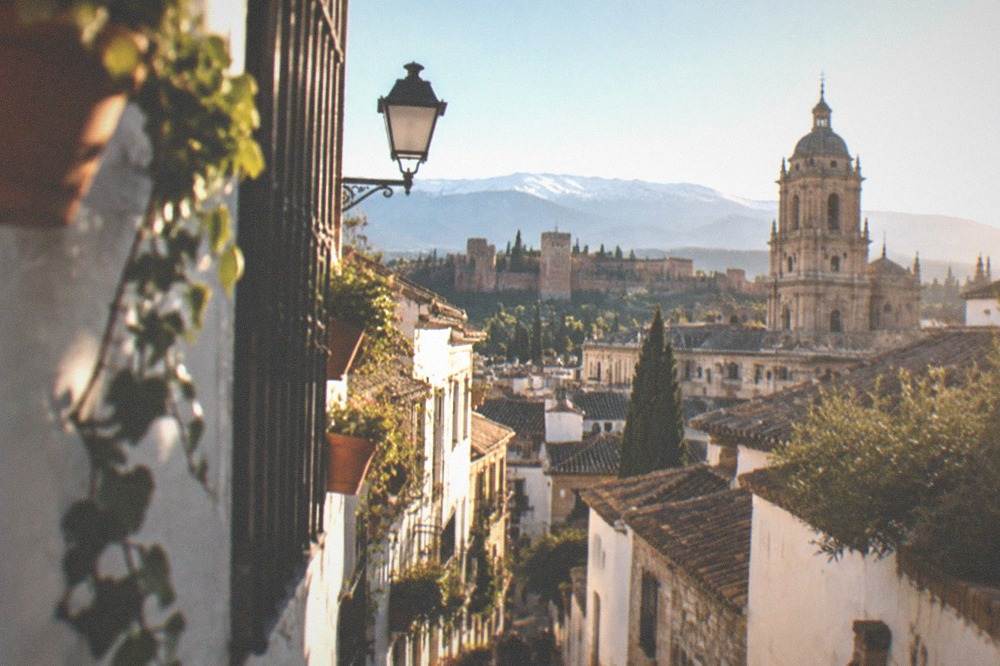 A historic Granada street with white-walled buildings and the cathedral tower rising above the rooftops