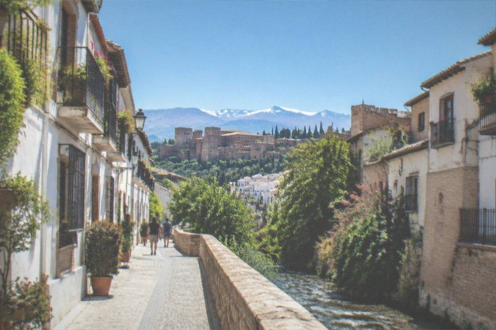 A narrow riverside street in Granada with old buildings rising on both sides