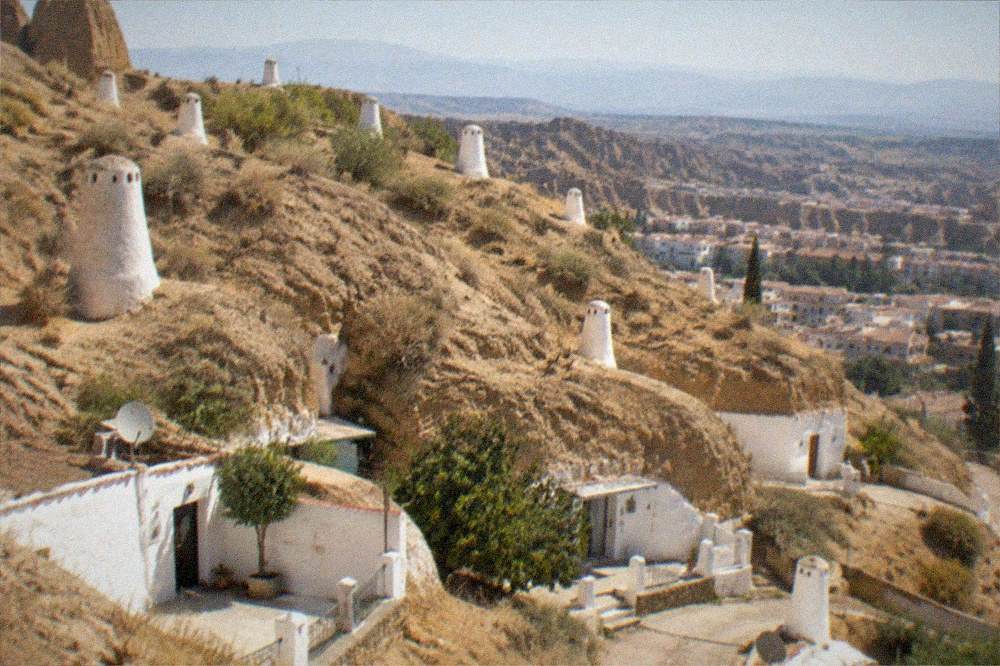 An illuminated hillside quarter of Granada at dusk with cave houses built into the rock