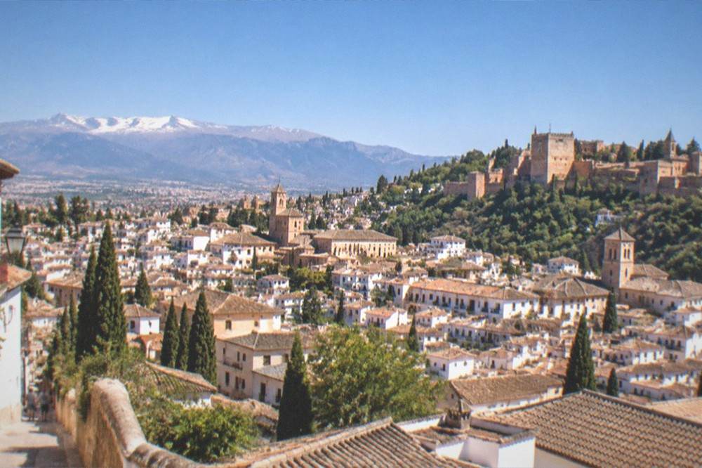 A wide cityscape of Granada with mountains rising behind the rooftops