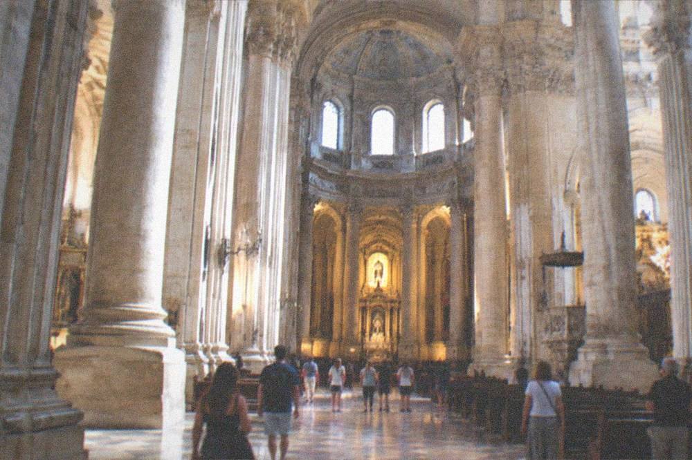 A grand renaissance church interior with tall columns and visitors walking through