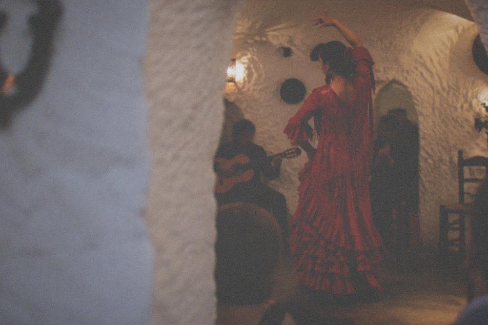 A flamenco dancer performing in a small whitewashed cave venue with warm lighting