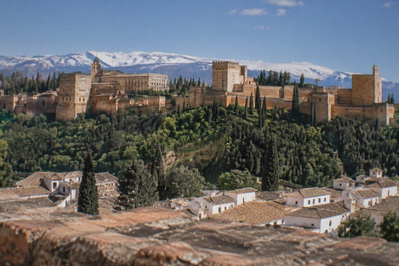 The Alhambra palace complex on its hill above the red-tiled roofs of Granada with the Sierra Nevada in the background