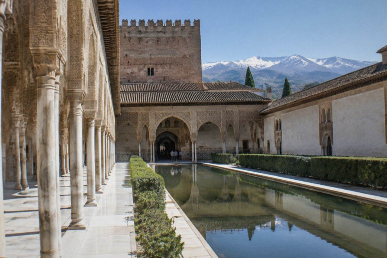 The Nasrid Palaces of the Alhambra seen from a hillside path with the Sierra Nevada in the background